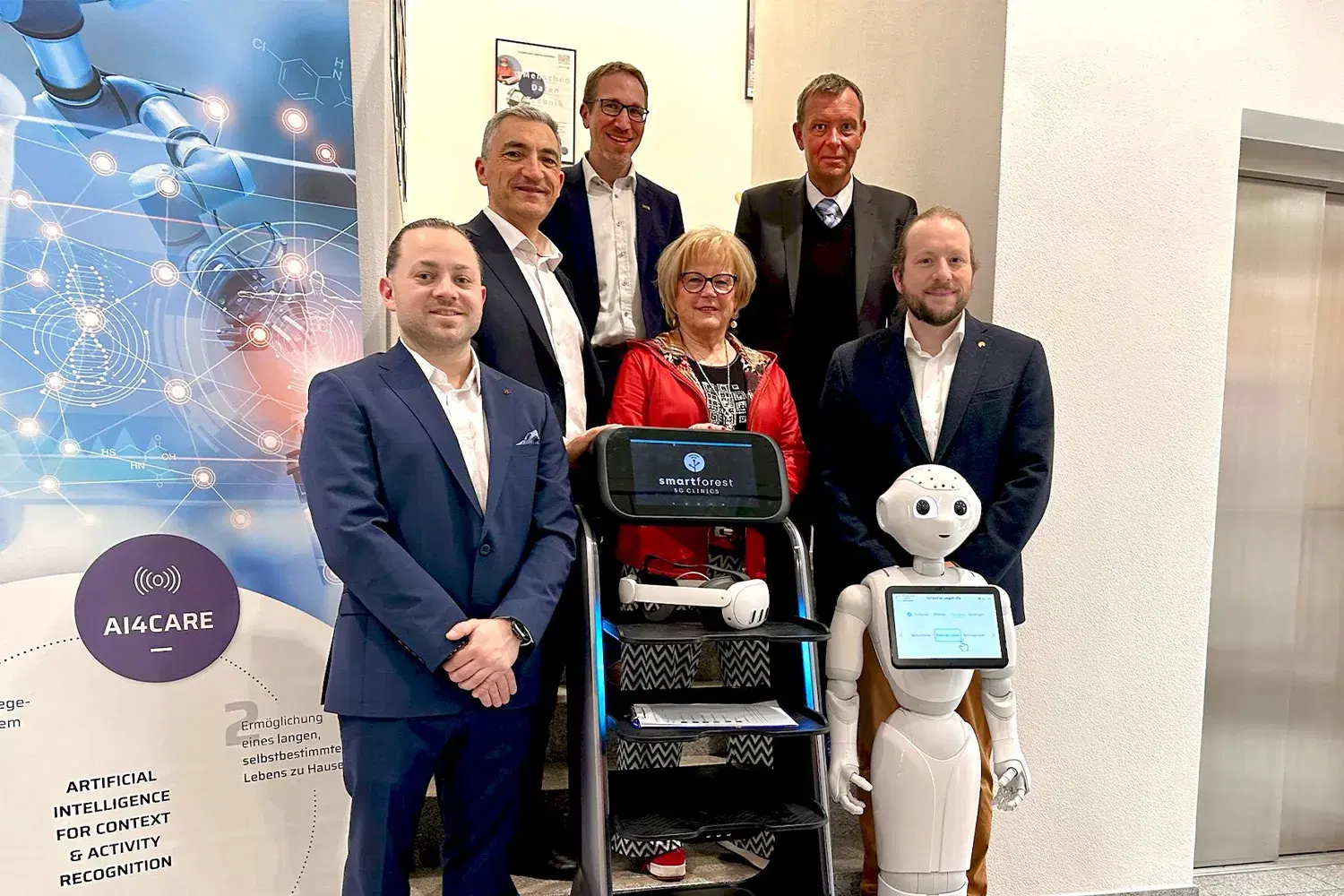 Group photo of six people on a staircase, in front a delivery robot showing the SMART FOREST 5G Clinics logo on its display and a humanoid robot with a tablet